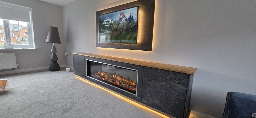 Lit fire built into a dark cabinet with a timber top and warm lighting beneath