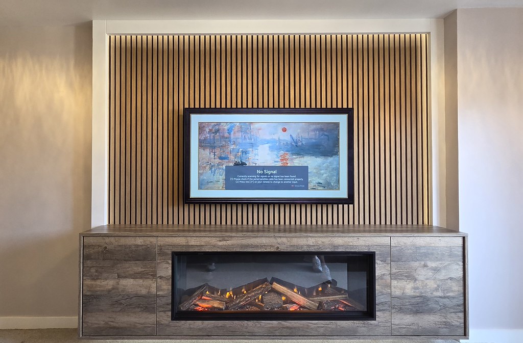 Electric fire set into wood-effect cabinetry with cupboards either side and slatwall above